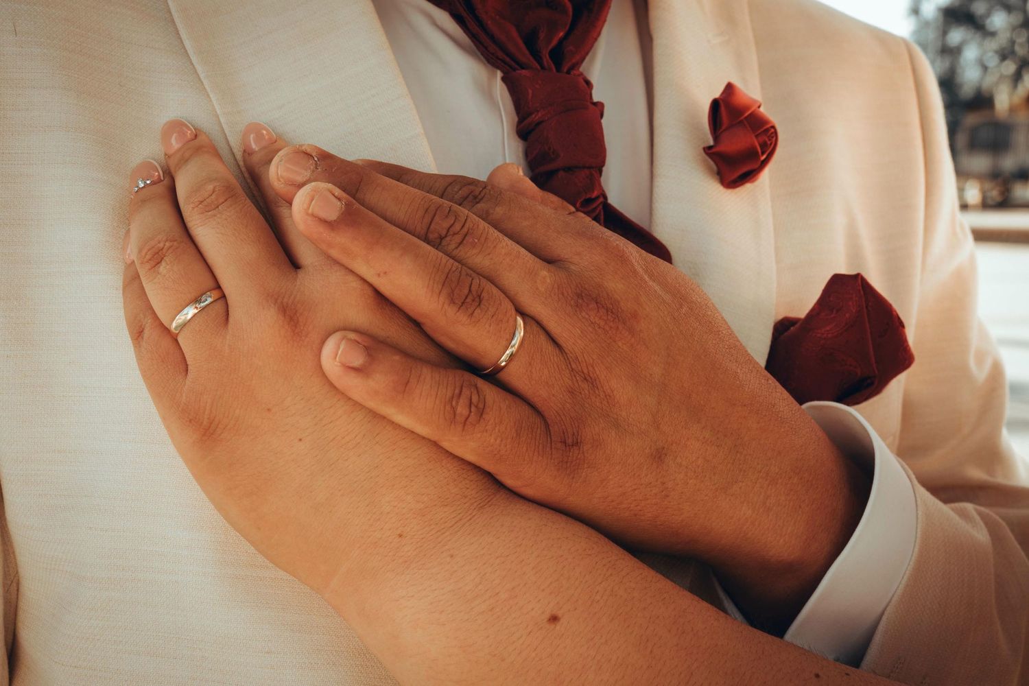 Primer plano de manos con anillos de matrimonio sobre fondo de tela blanca.