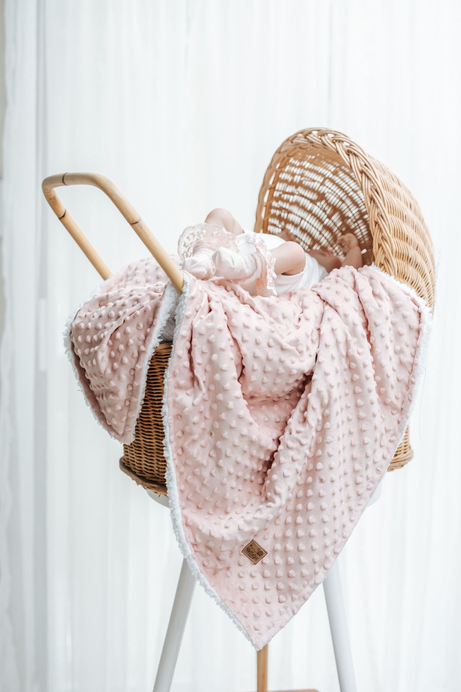 Pink minky dot baby blanket draped over a wooden rocking chair against a white curtain background.