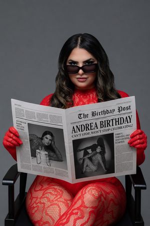 Woman in red lace outfit and sunglasses reads The Birthday Post newspaper celebrating Andrea's birthday while seated in a chair.