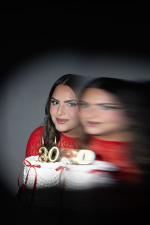 Woman in red lace dress celebrating 30th birthday with white cake and gold number candles, motion blur effect.
