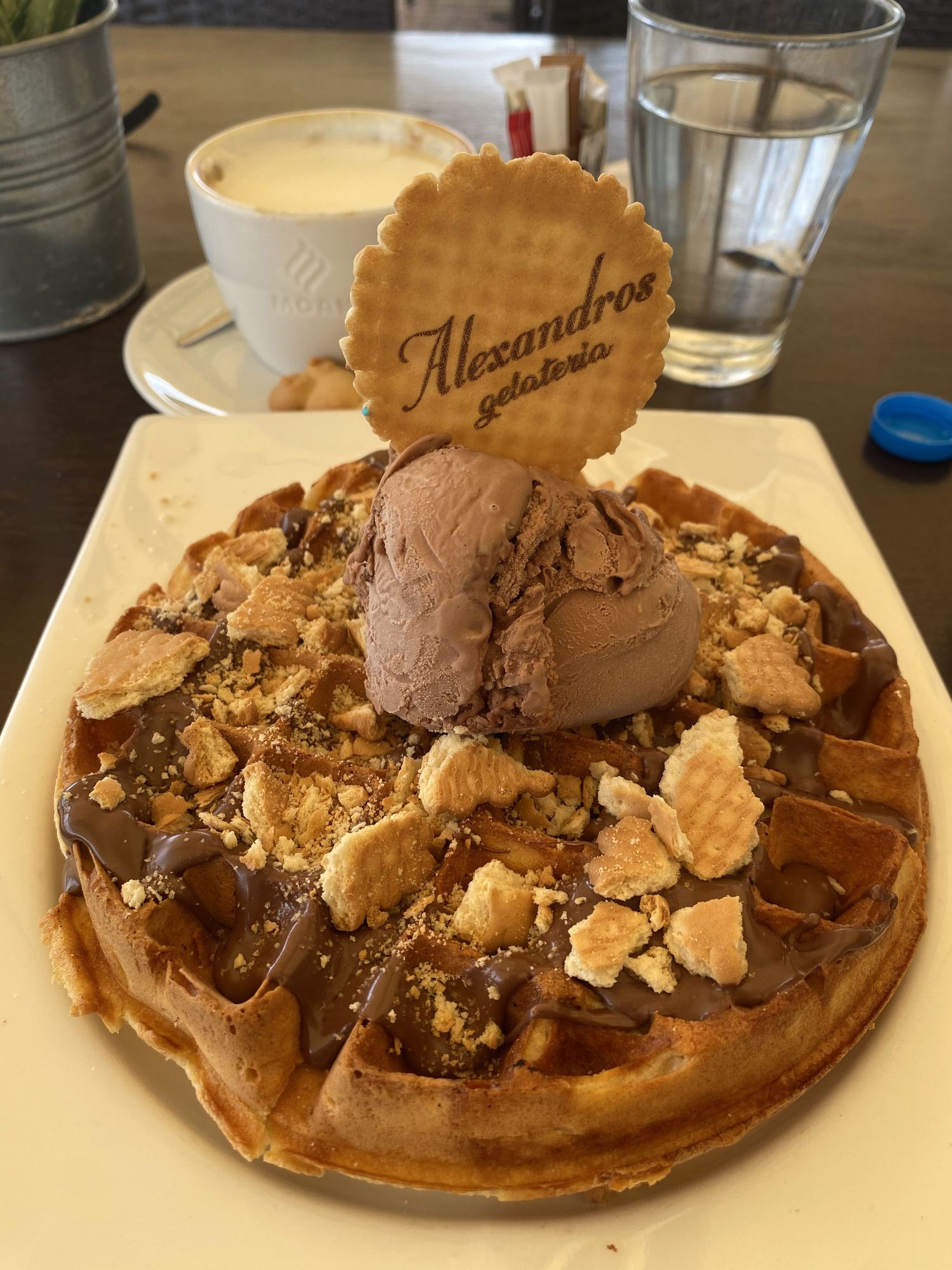 A chocolate waffle topped with ice cream, chocolate sauce, and cookie crumbles served on a white plate.