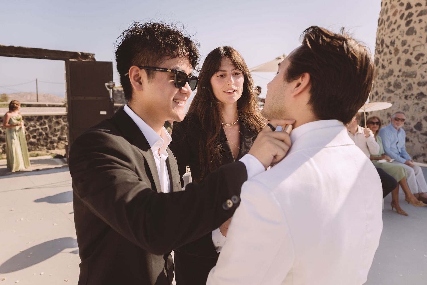 A groomsman at a destination wedding in Santorini attends to the groom.