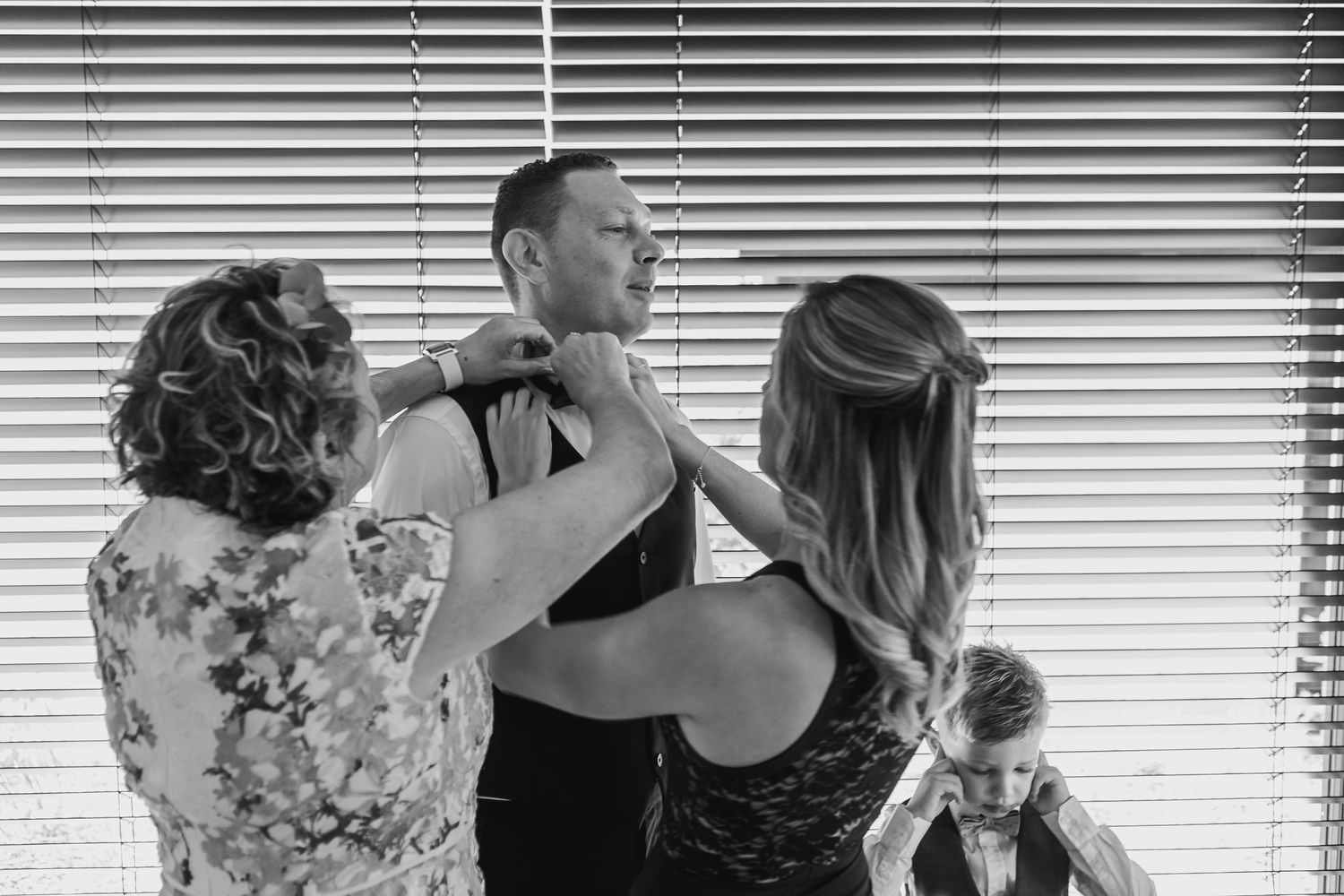 Wedding preparation scene with formal attire adjustments in black and white.