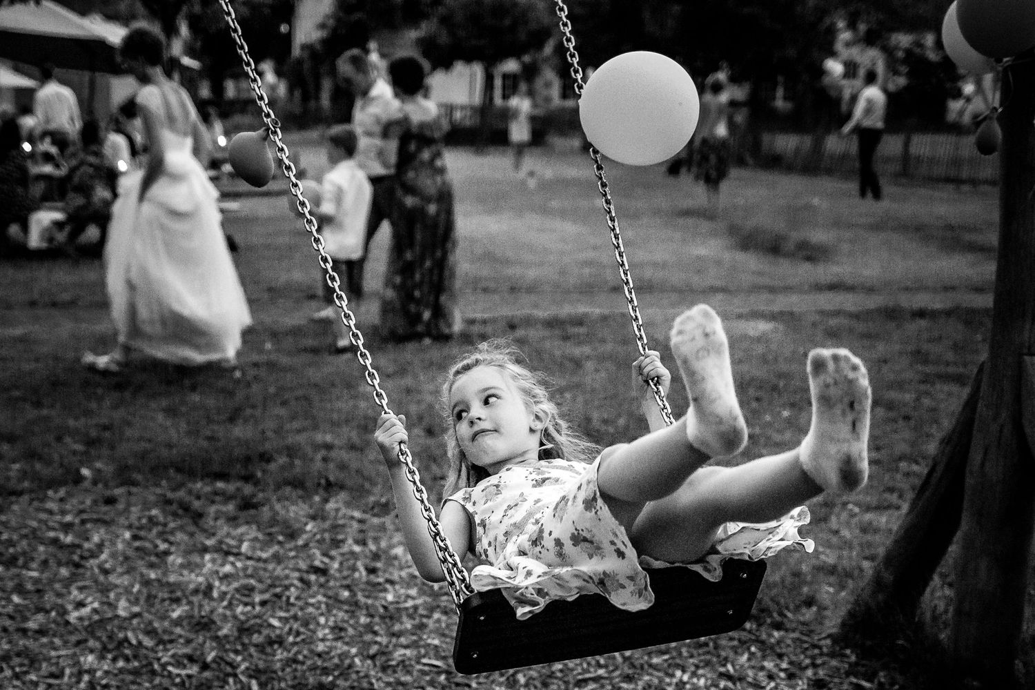 Child swinging joyfully with a balloon in a black and white candid moment.