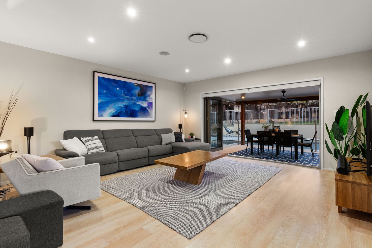 Bright living room with grey sofas, timber coffee table, light floors, and outdoor entertaining access.