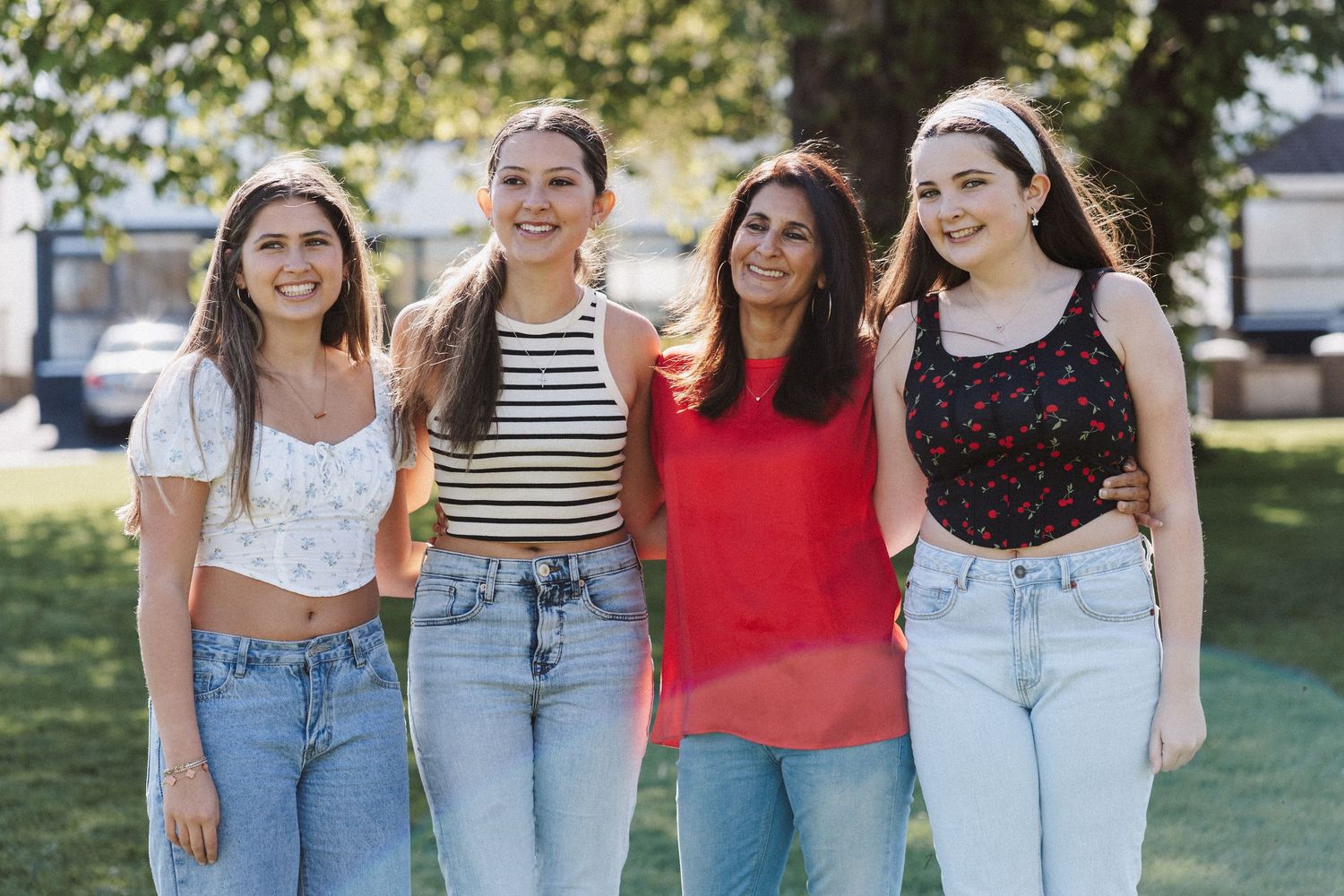 A group of friends wearing casual summer outfits with jeans and t-shirts pose together outdoors on a sunny day.