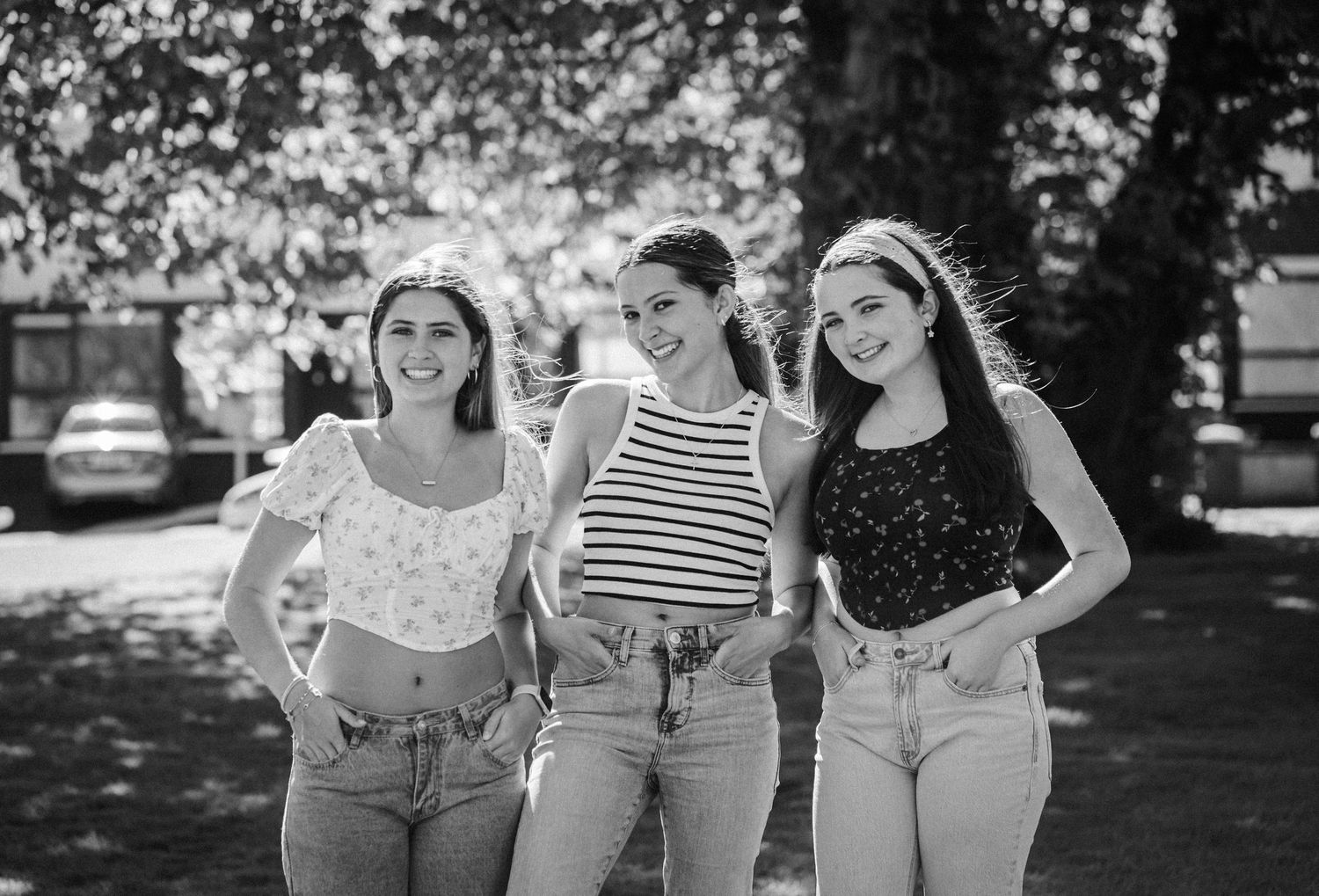 A group of people wearing casual summer outfits walk together outdoors in a park setting.