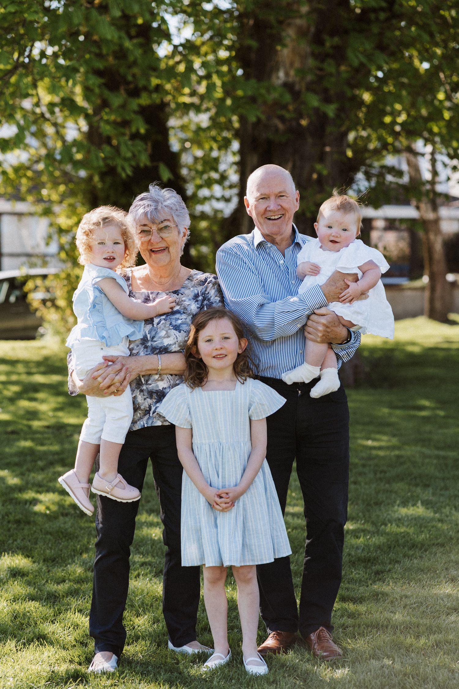 Family members in coordinated blue and white outfits pose together on sunny grass for outdoor portraits.