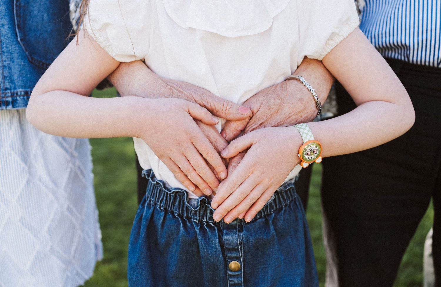 Close-up view of hands resting on a denim skirt with white lace top and gold watch details.