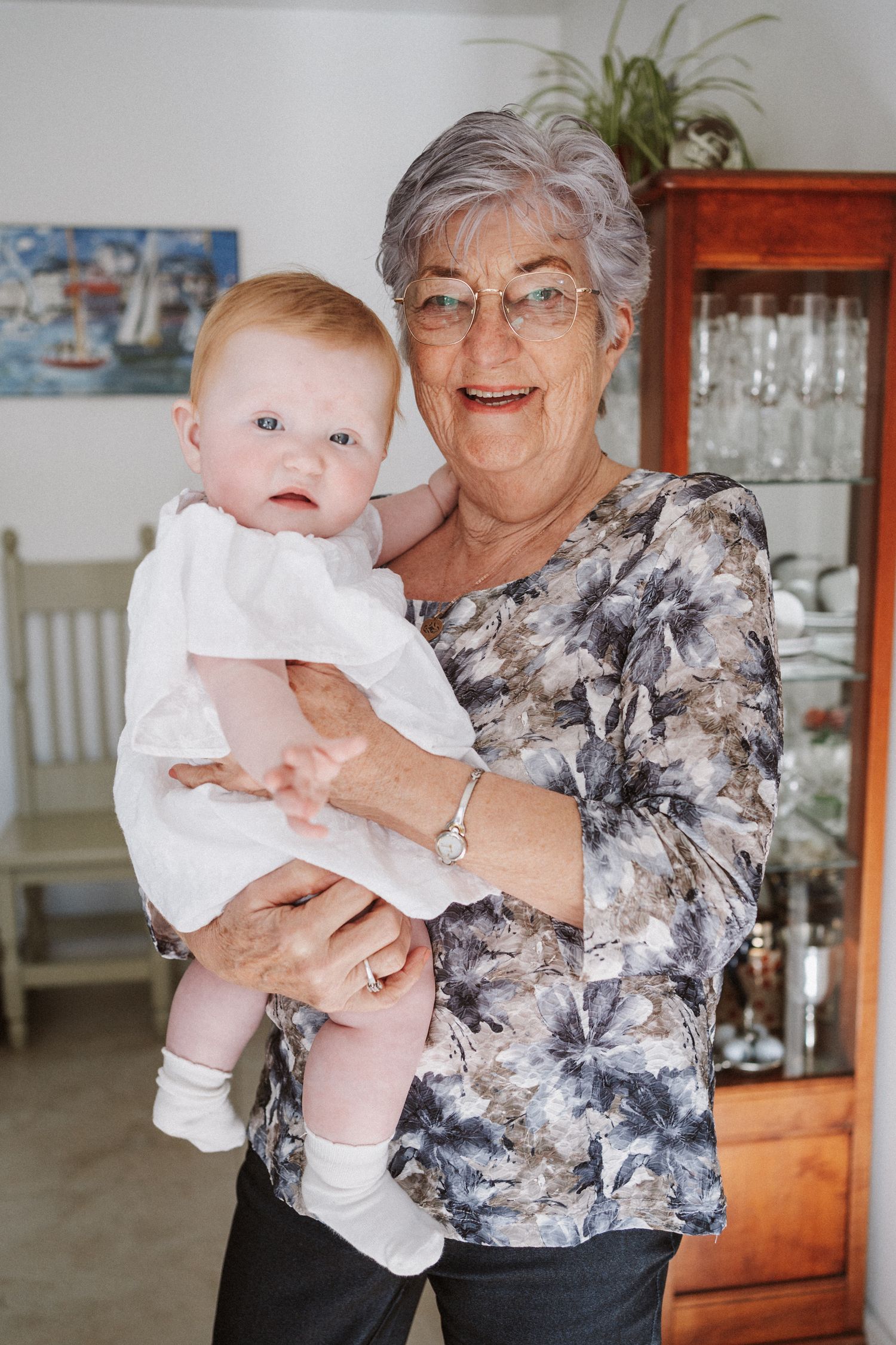 A series of four connected photos showing a baby in white clothing being held in what appears to be a home setting.