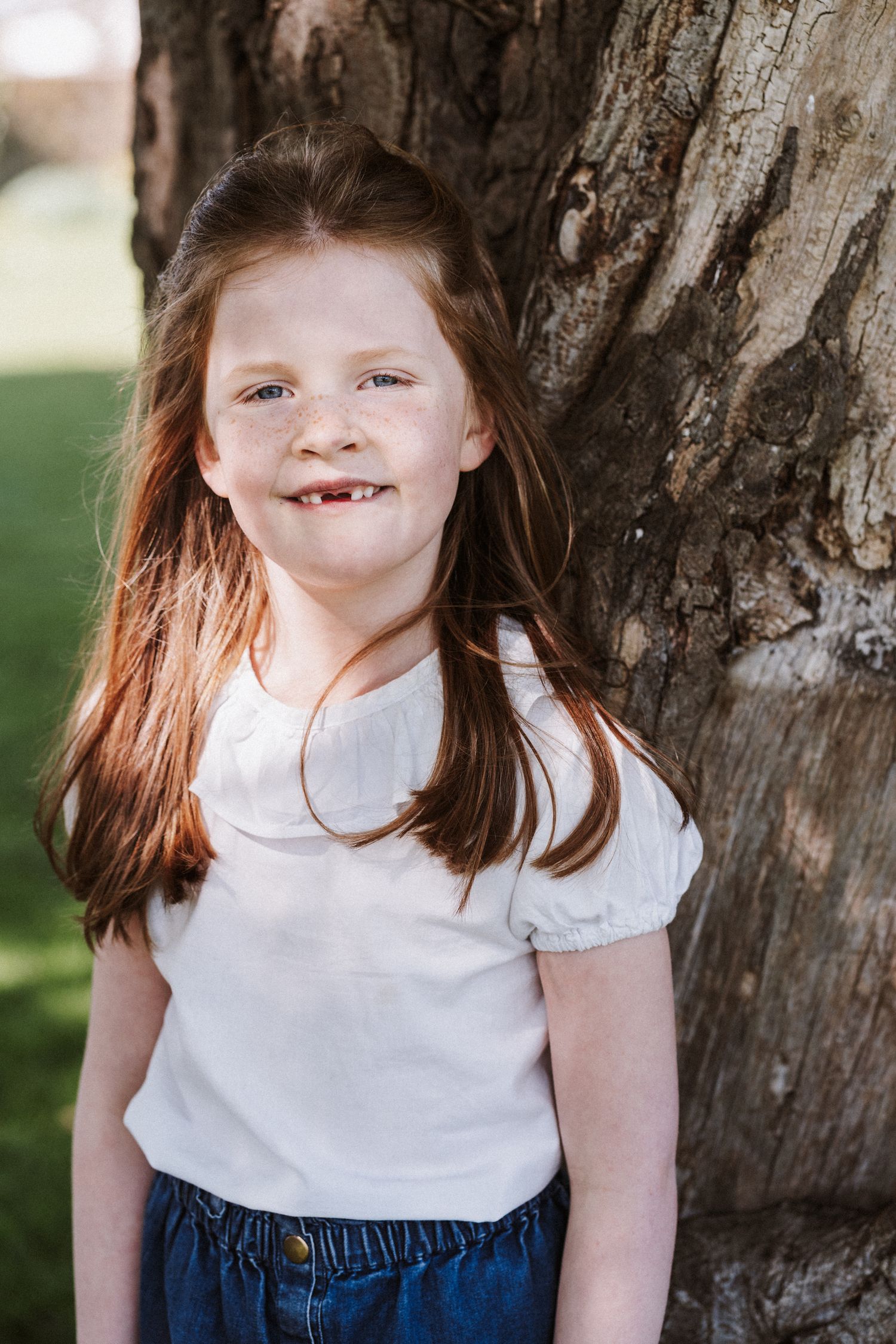 Child wearing white top and denim in outdoor spring portrait session.