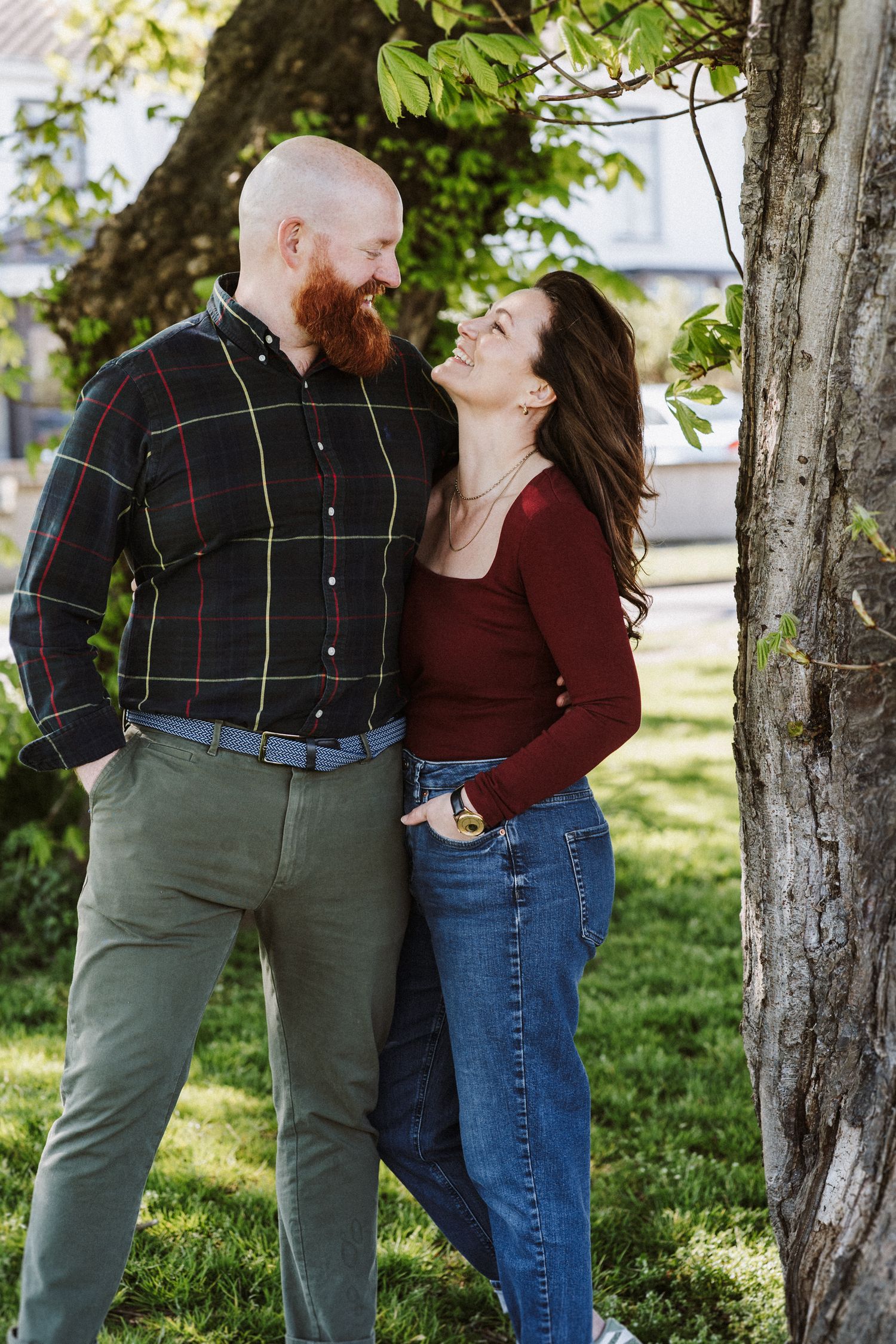 A couple shares a romantic moment outdoors under green trees on a sunny day.
