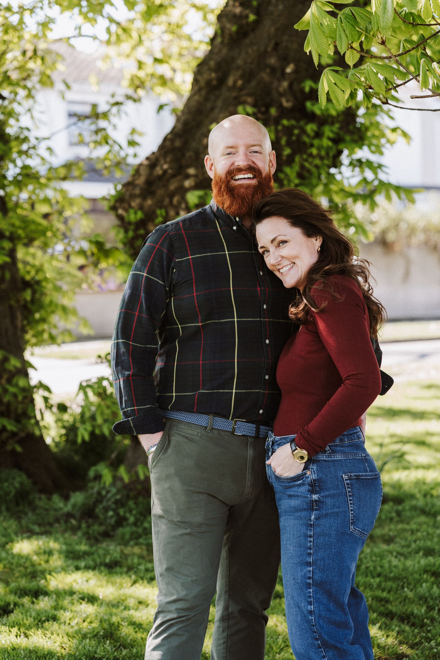 A joyful couple embraces while taking outdoor photos in a natural setting with sunlit foliage.