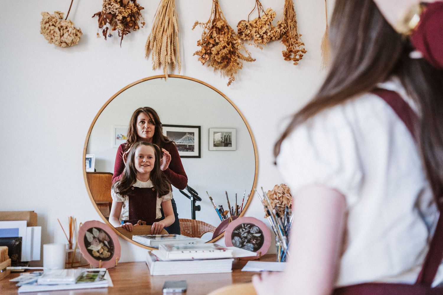 A series of five photos showing an artist working at a desk with dried flowers and embroidery materials.