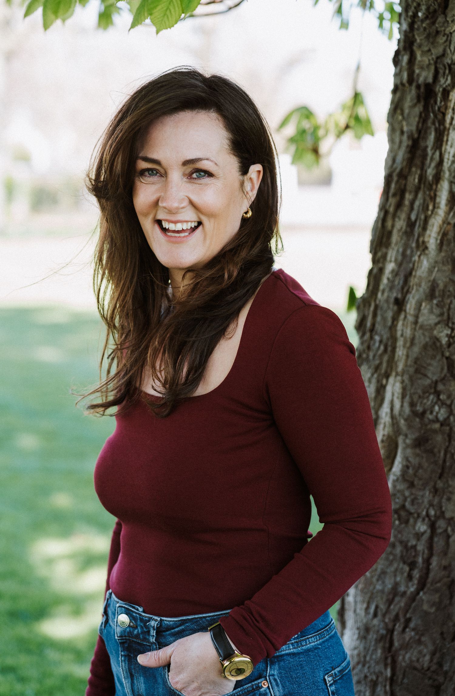 A person in a burgundy sweater and jeans poses outdoors near trees in a casual photo series.