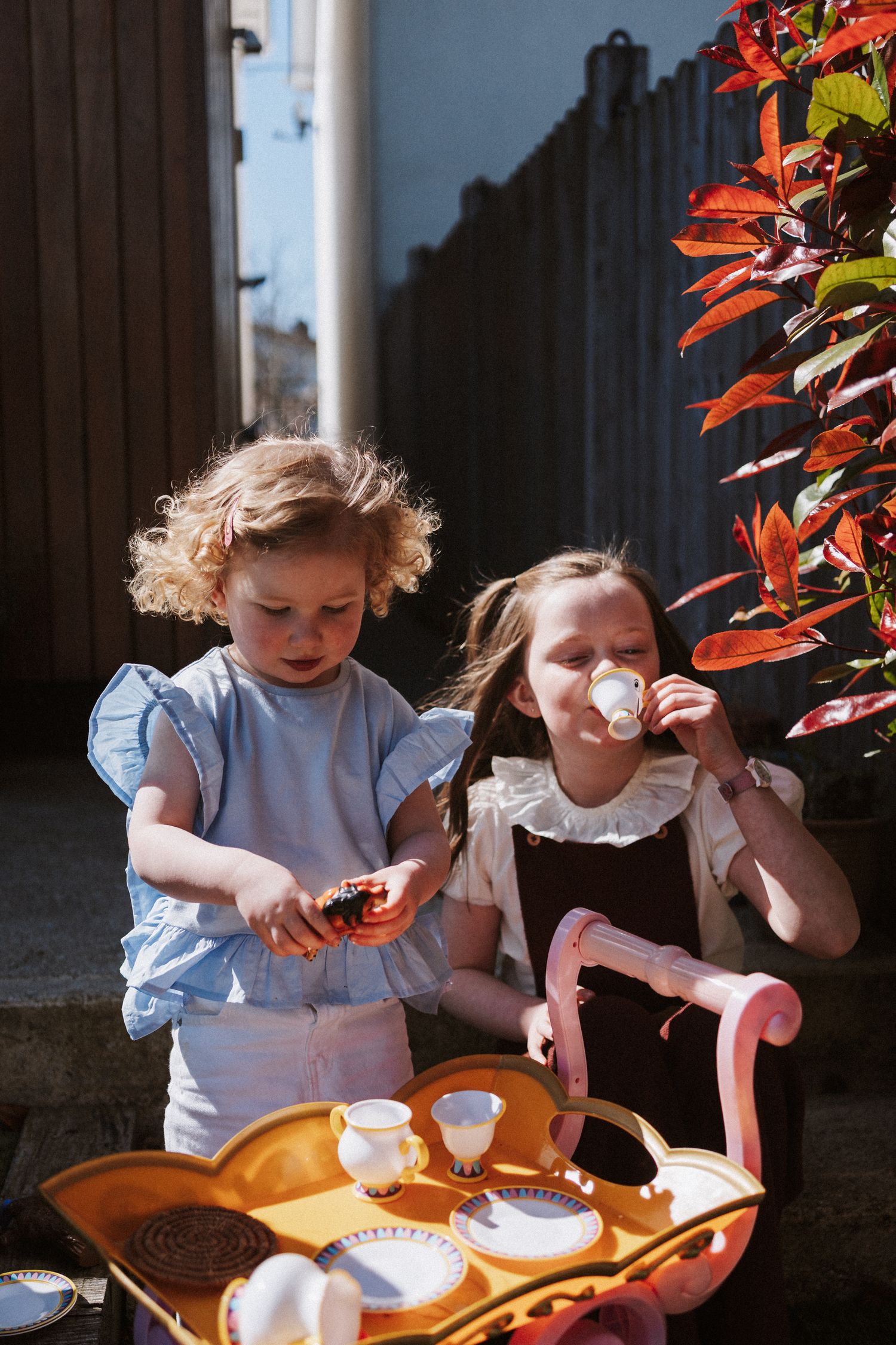 Two children enjoy a sunlit tea party with small cups and snacks in a garden setting.