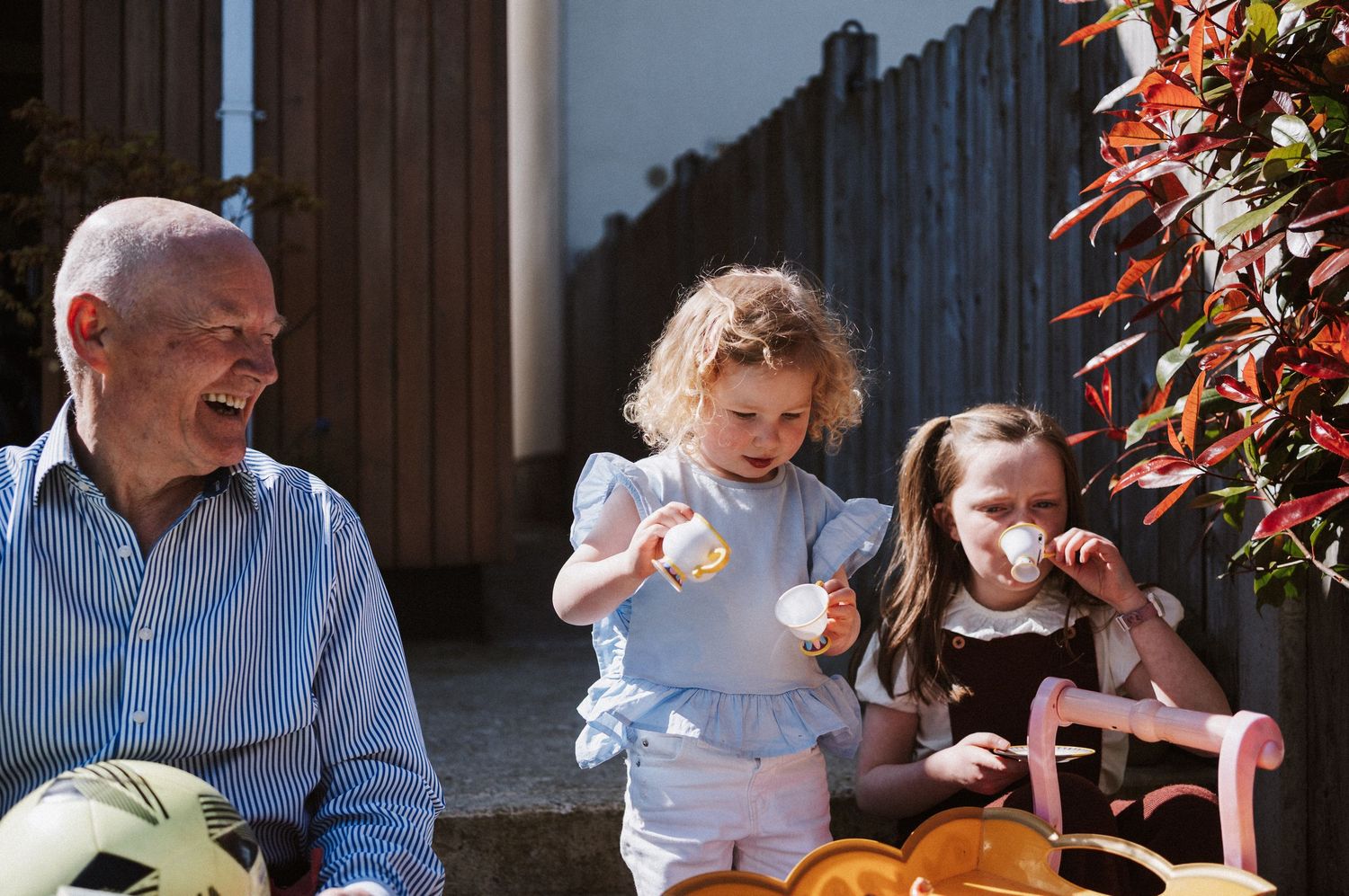 A group of people enjoying a meal together outdoors on a sunny day with colorful flowers in the background.