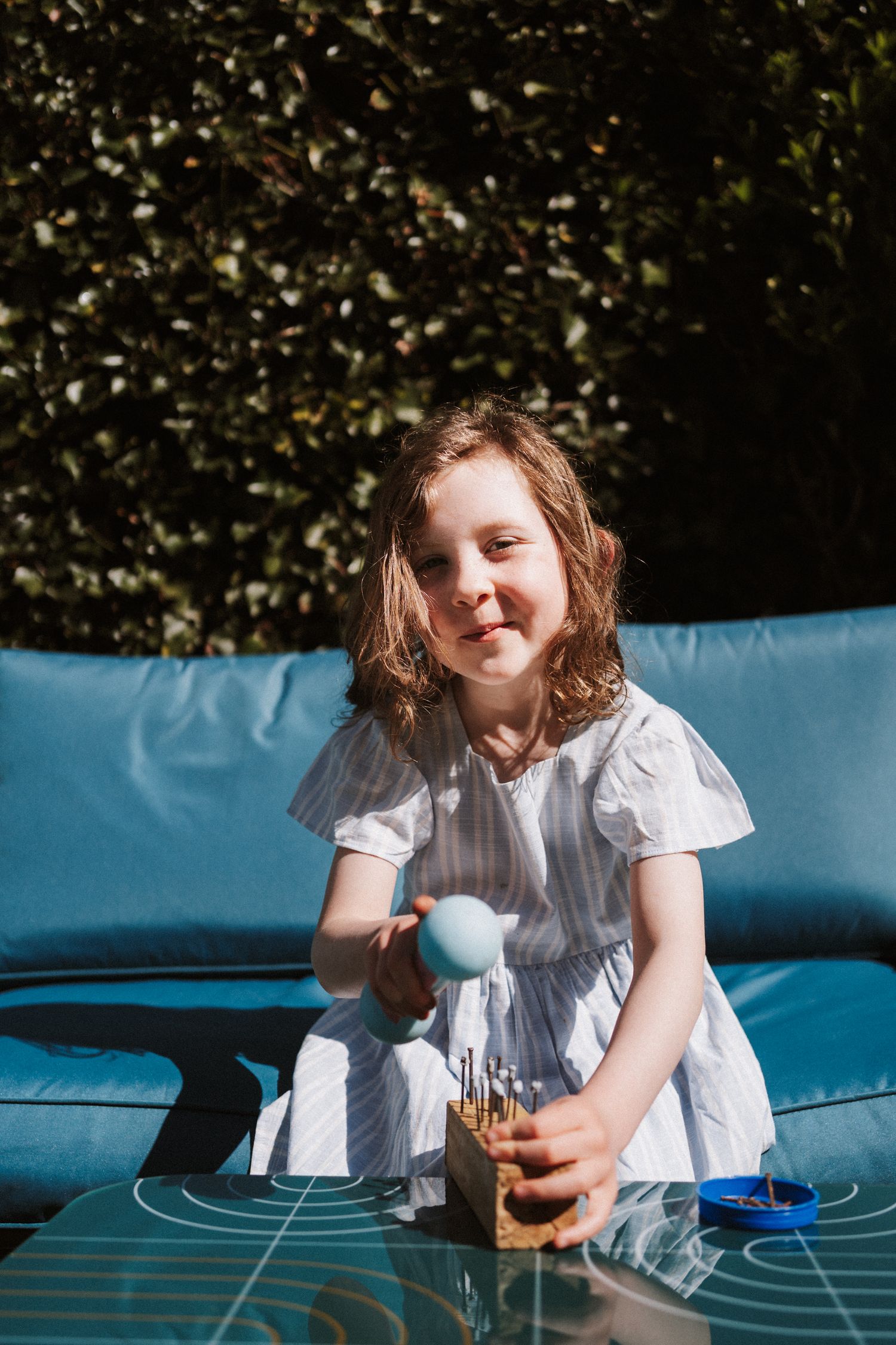 A child in a white dress plays on a blue trampoline on a sunny day.