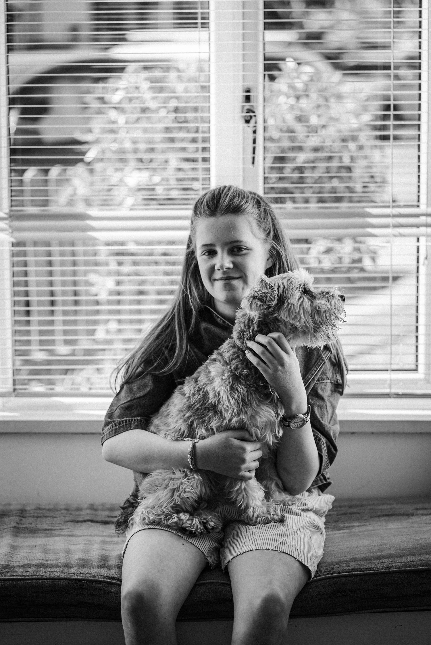 Black and white photo series showing a child sitting by a window with a small fluffy dog in four sequential moments.