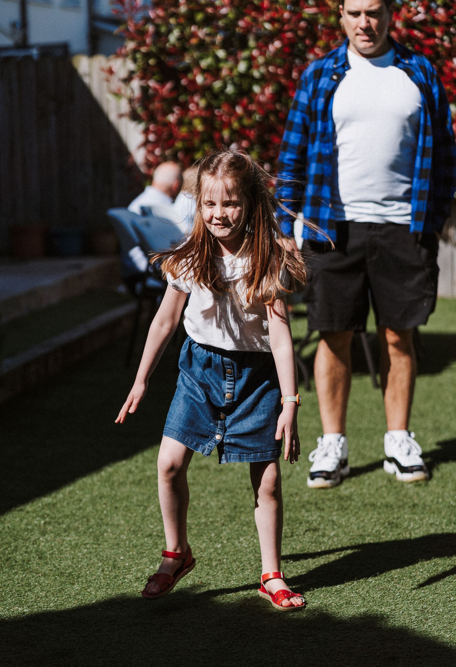 Child playing and running on green artificial turf in casual denim and white outfit during outdoor activity.
