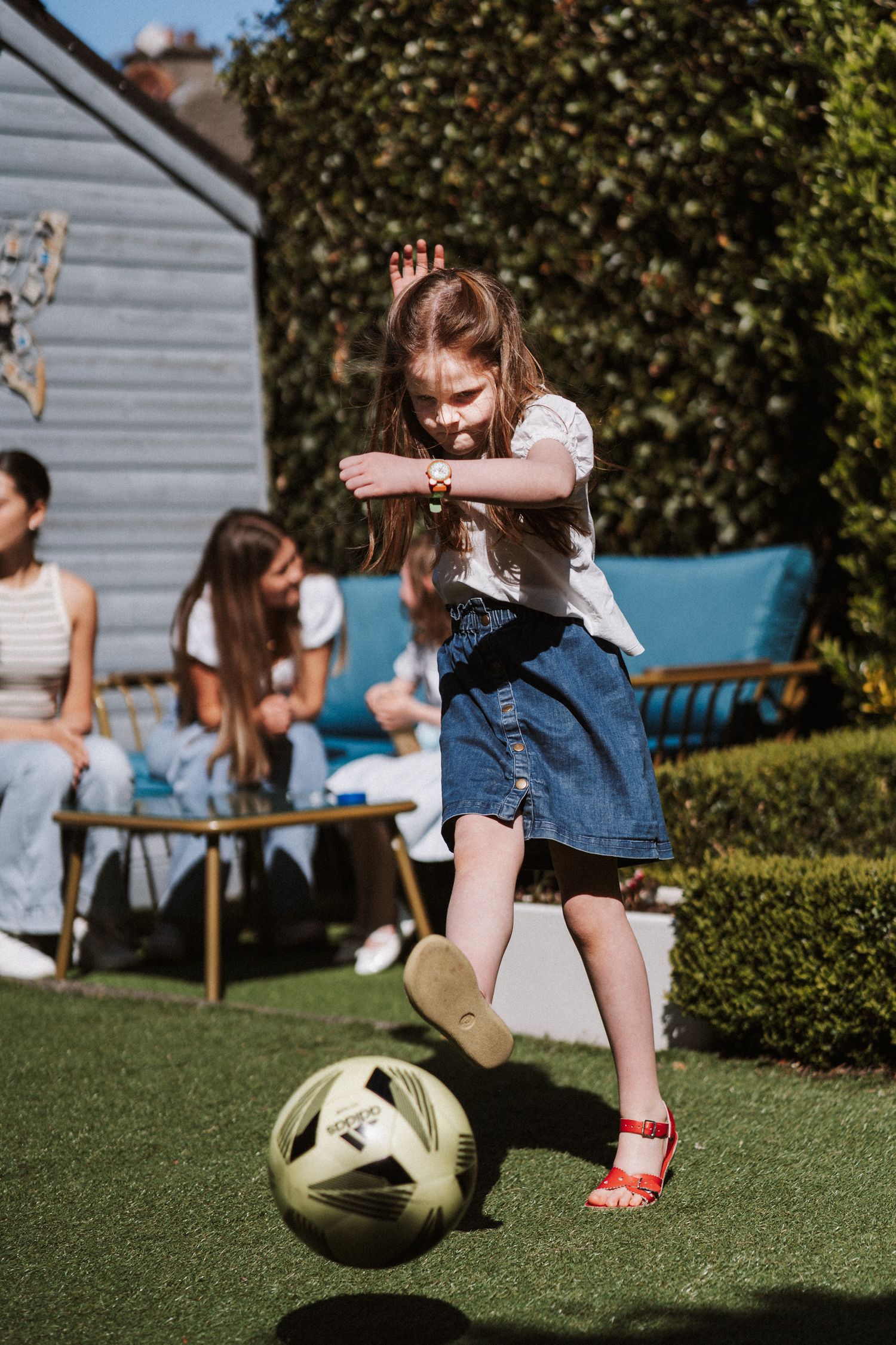 A sequence of action shots showing someone kicking a soccer ball on a sunny lawn with benches in the background.