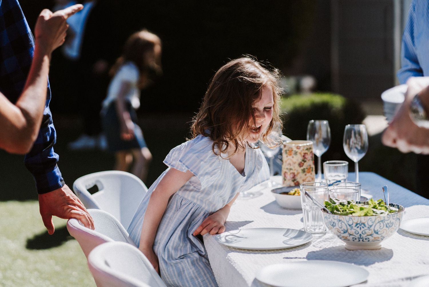 Guests dining outdoors at an elegant garden party with white tablecloths and wine glasses.