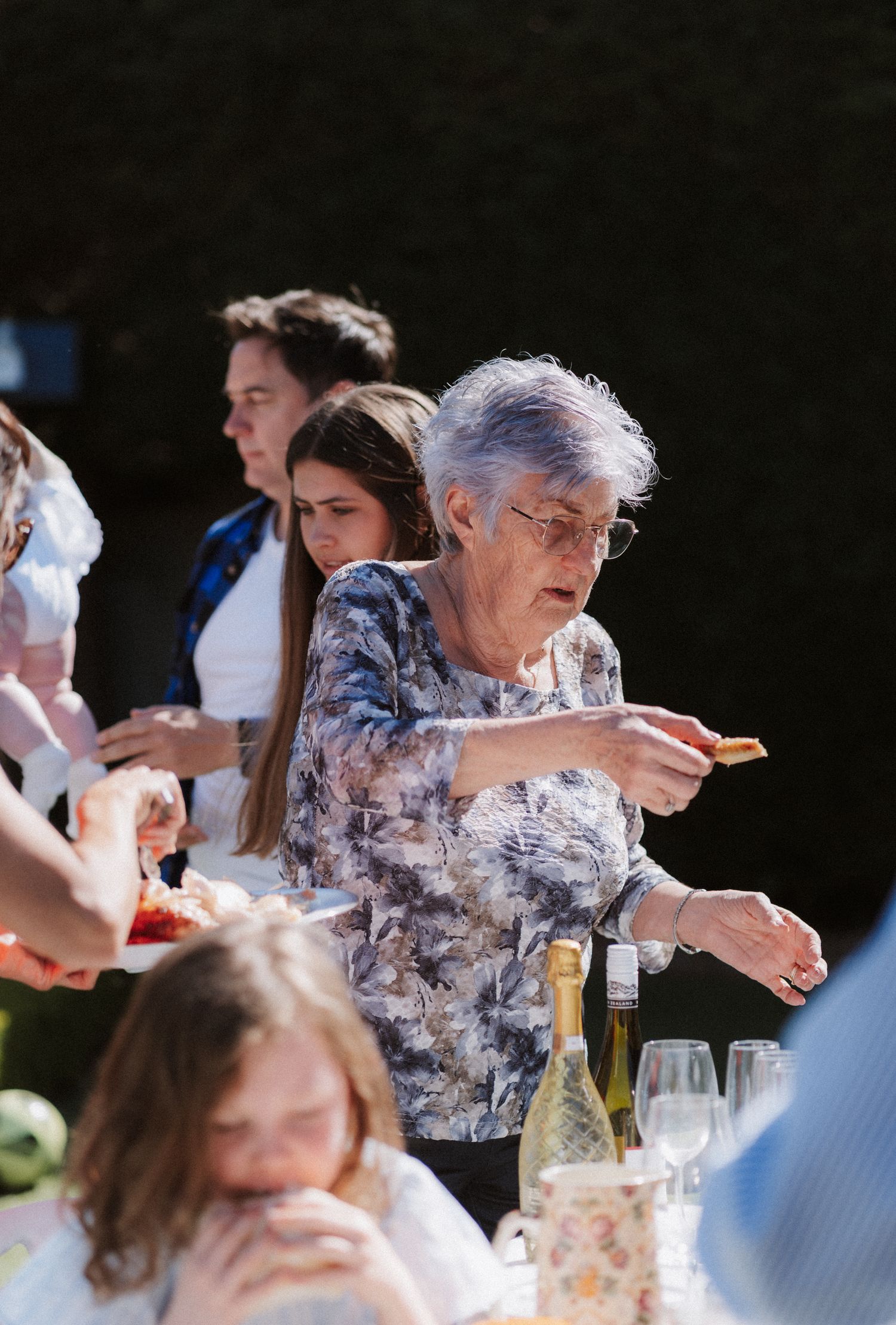 People gathered at an outdoor dining event with wine glasses and conversation under natural lighting.