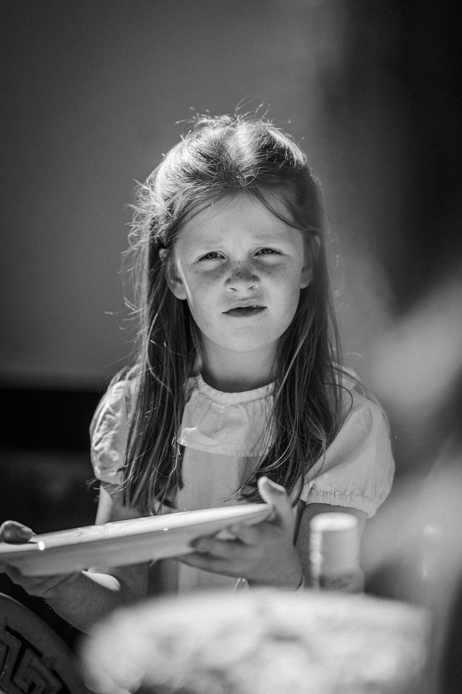 A black and white portrait of a child holding a book with sunlight creating a dramatic lighting effect.