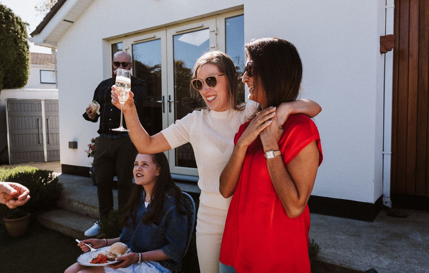 Group of friends relaxing and socializing outdoors on a sunny porch with drinks.