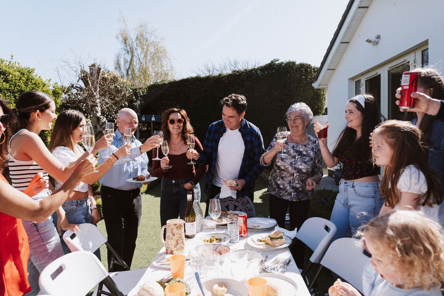 A group of people gathered outdoors for a casual social event with drinks and conversation on a sunny day.