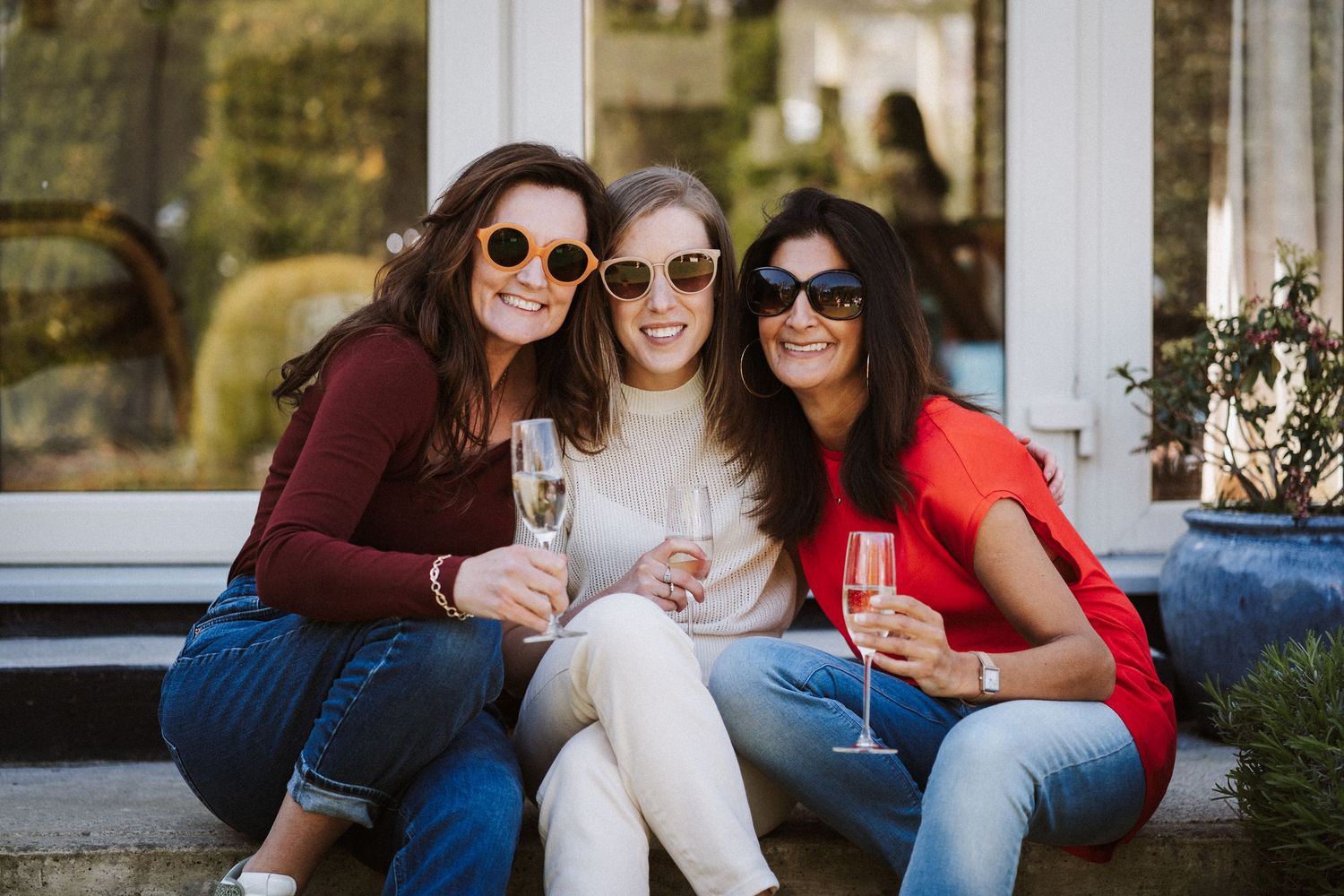 Friends enjoying drinks and conversation while sitting together on an outdoor patio during a sunny afternoon.