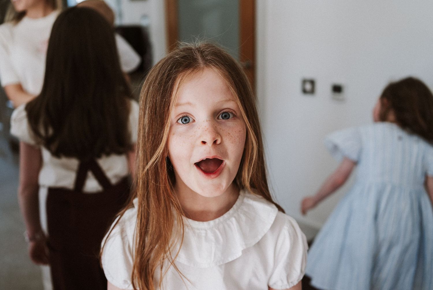 A young girl in a white dress makes an exaggerated surprised expression with bright red lipstick.