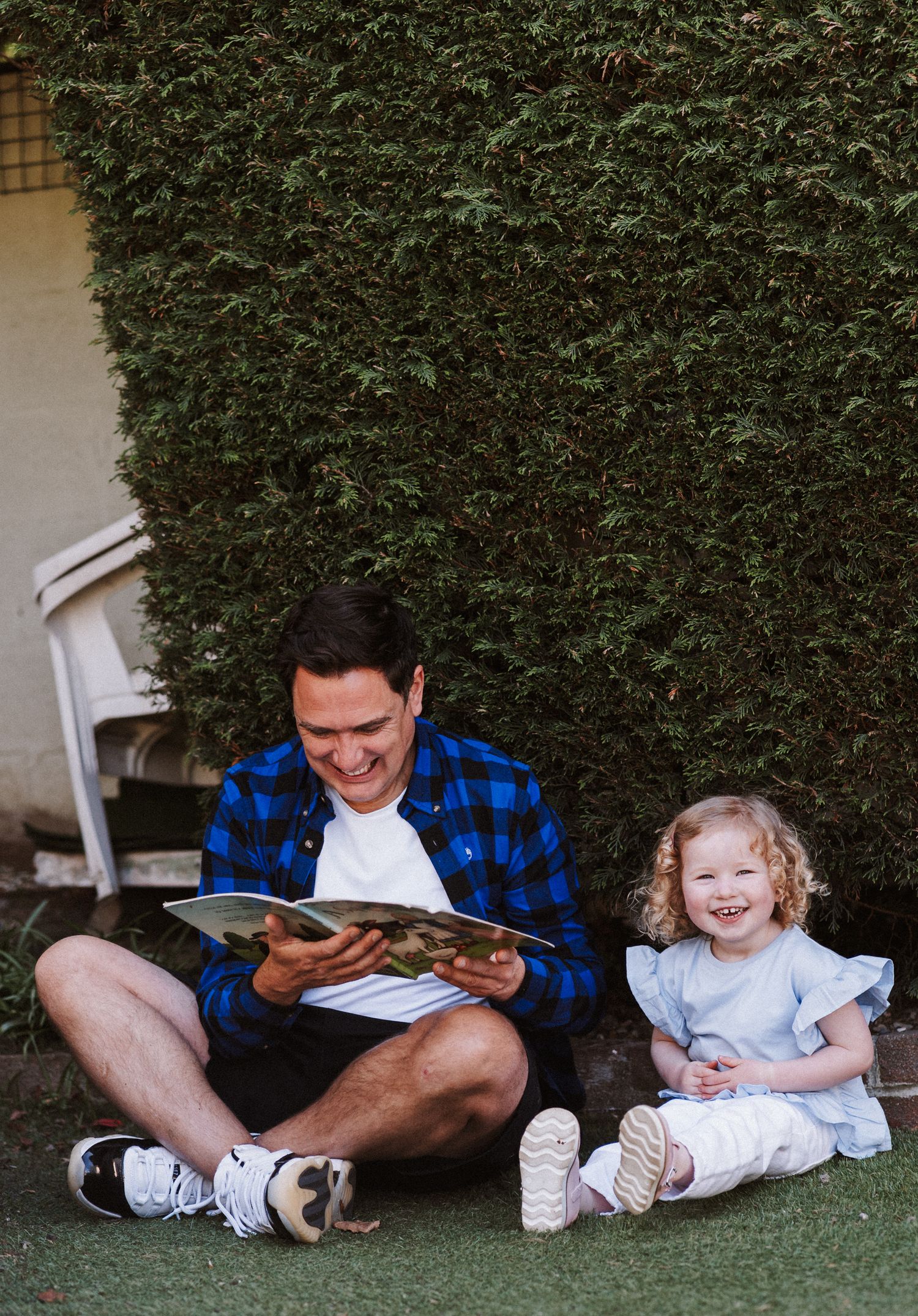 A parent and child sit together on artificial grass reading books and sharing a tender moment outdoors.
