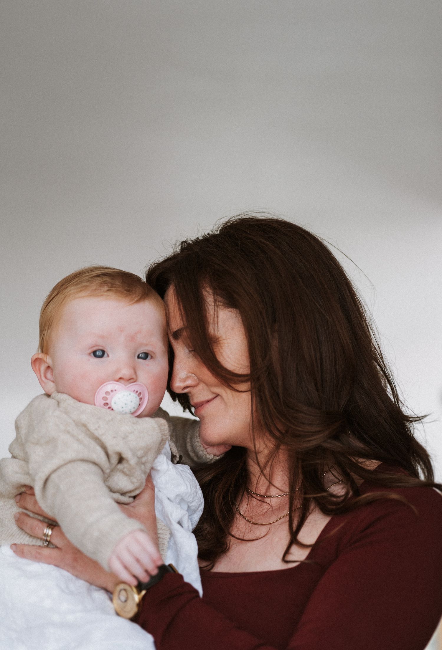 A tender moment captured between a parent and baby with a pacifier in a minimalist indoor setting.