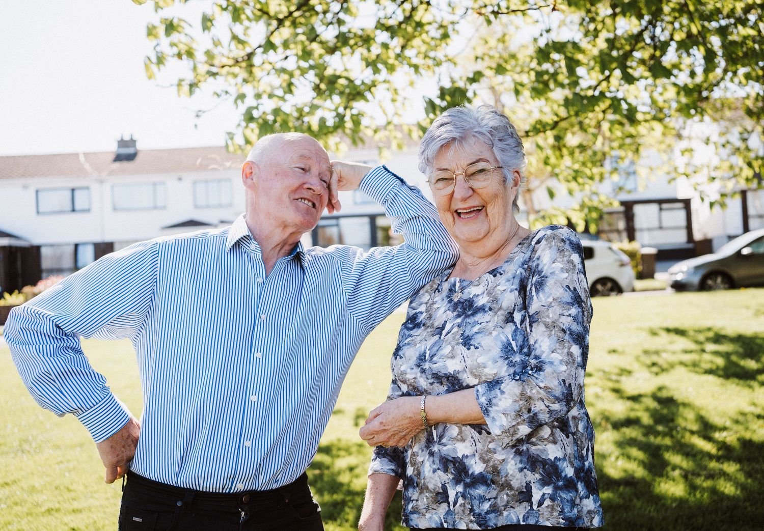 Senior couple laughing together outdoors on a sunny day in a residential neighborhood.