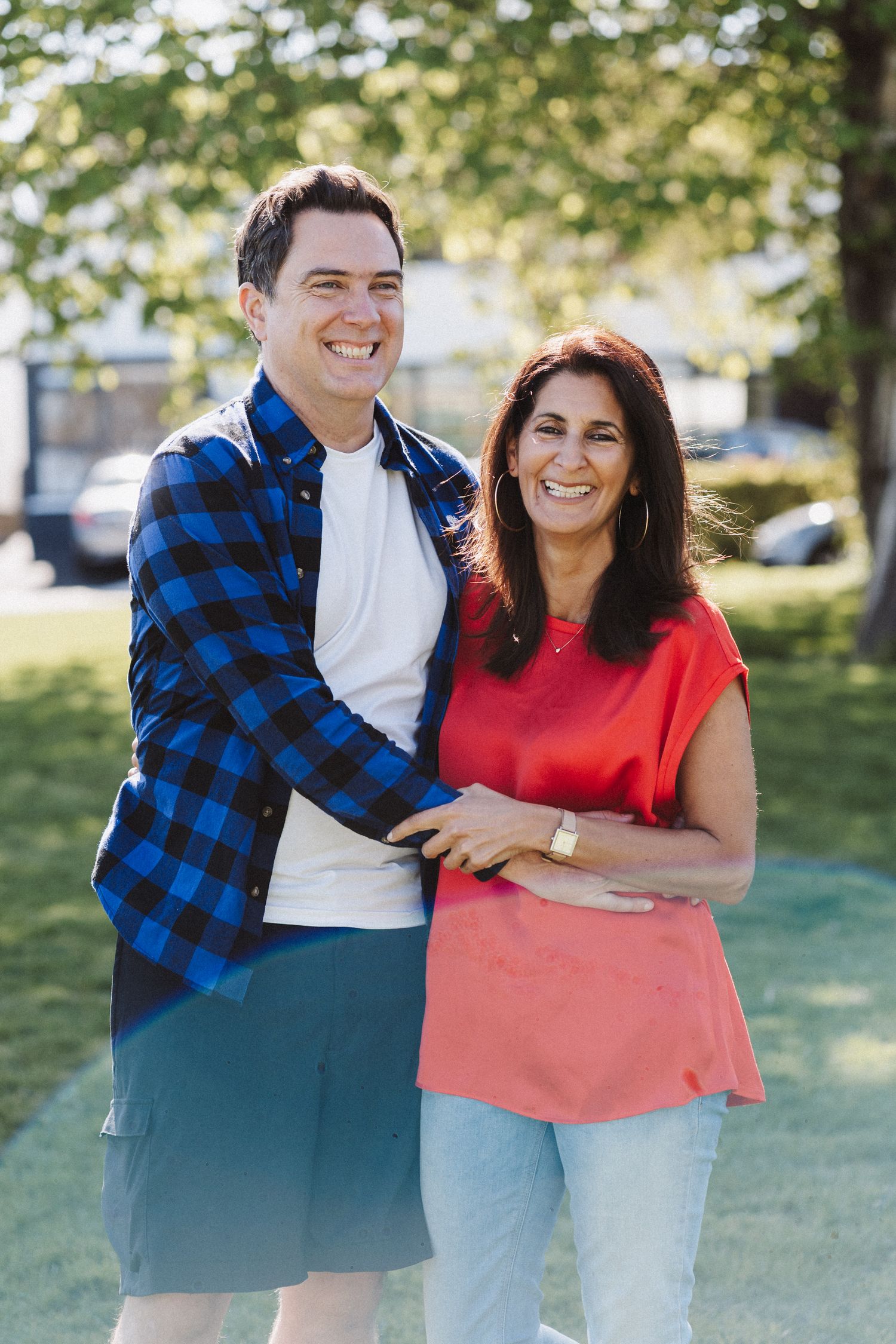 Two people share joyful moments outdoors while wearing casual attire in a sunny park setting.