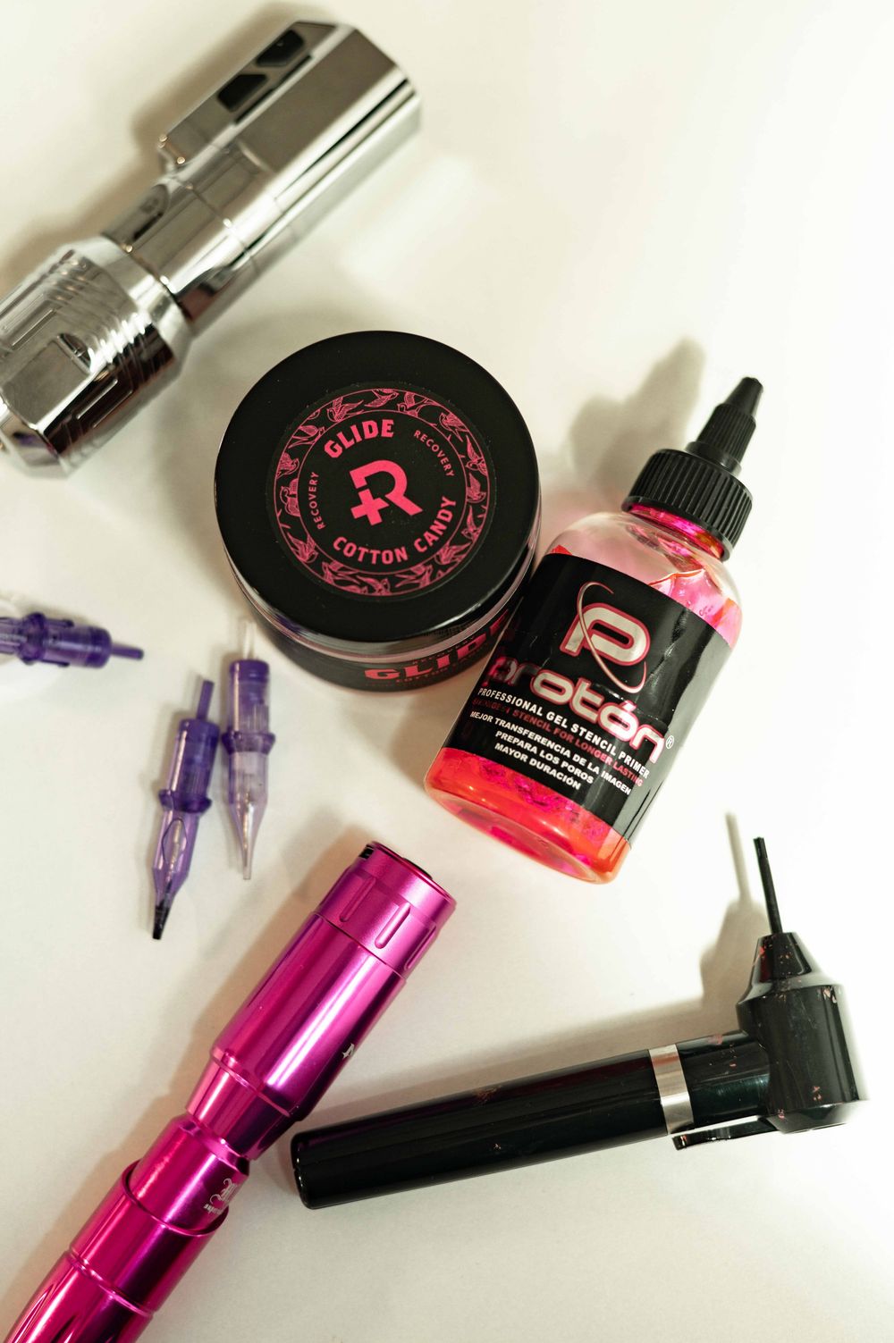 Various pink and black beauty tools and products including nail polish and makeup items scattered on a white surface.