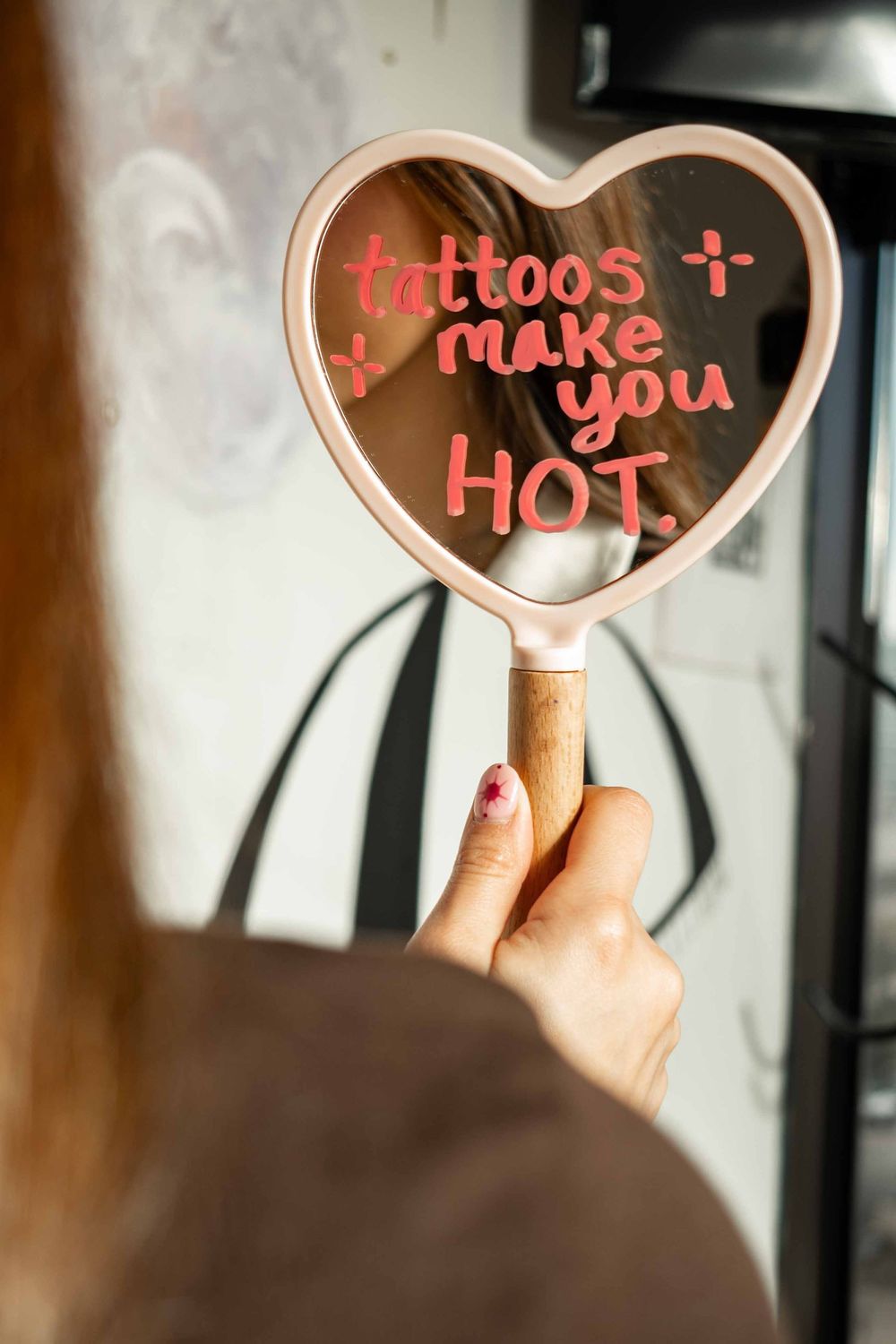 A sequence of heart-shaped mirrors reflecting handwritten text about tattoos and makeup in pink lettering.