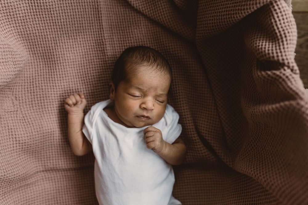 Newborn baby sleeping peacefully on dusty pink textured blanket with eyes closed and serene expression.