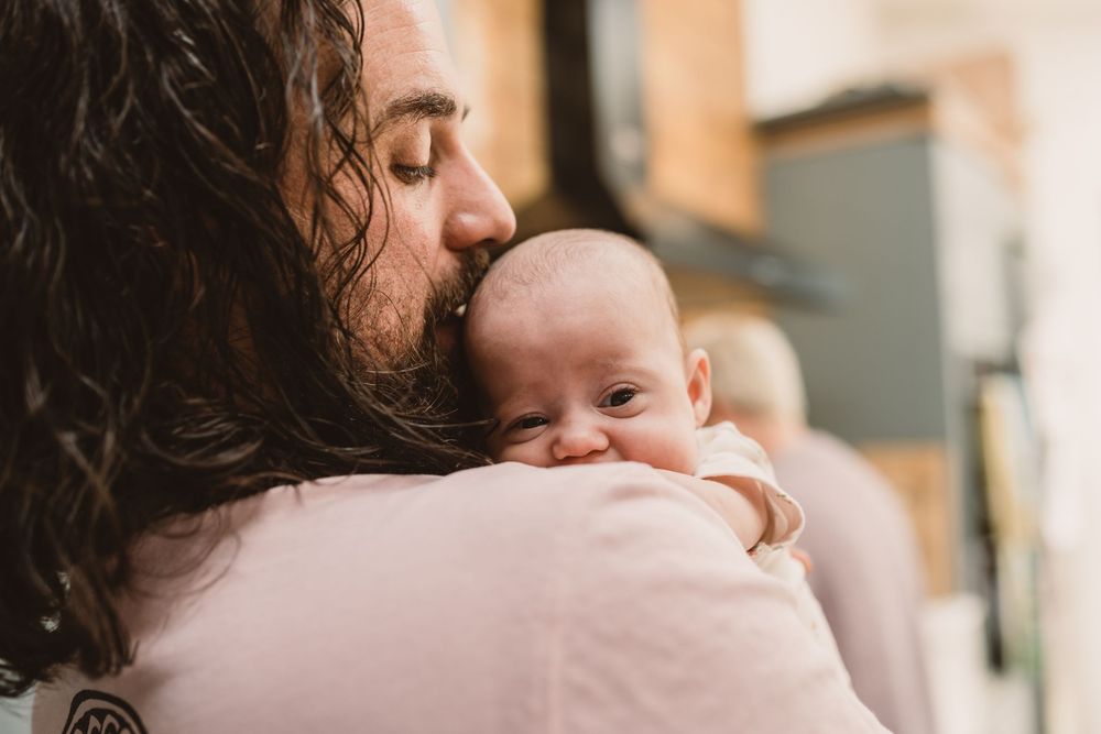 A father tenderly kisses newborn baby in natural light.