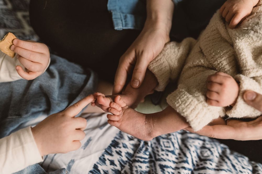 Hands gently hold a newborn baby's feet on a blue and white patterned blanket.