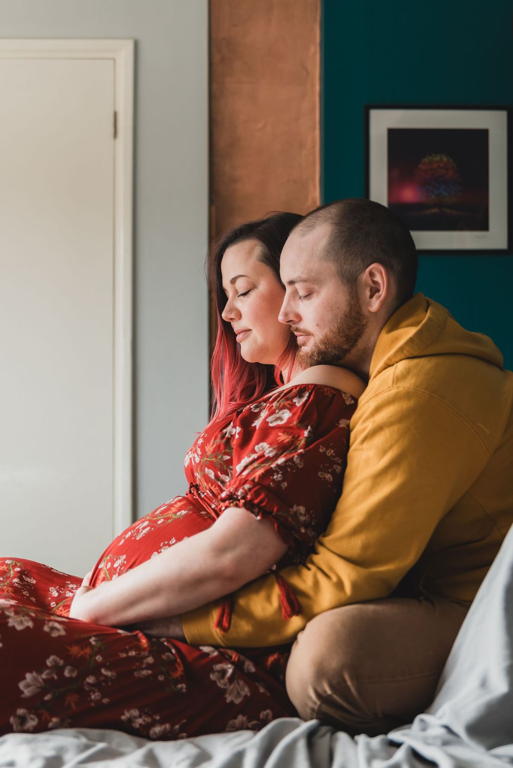 A couple in colourful clothes rests together in bed holding the woman's pregnant belly.