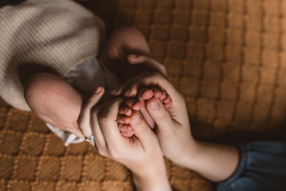 Close-up view of newborn baby feet being gently held by adult hands on a textured brown surface.