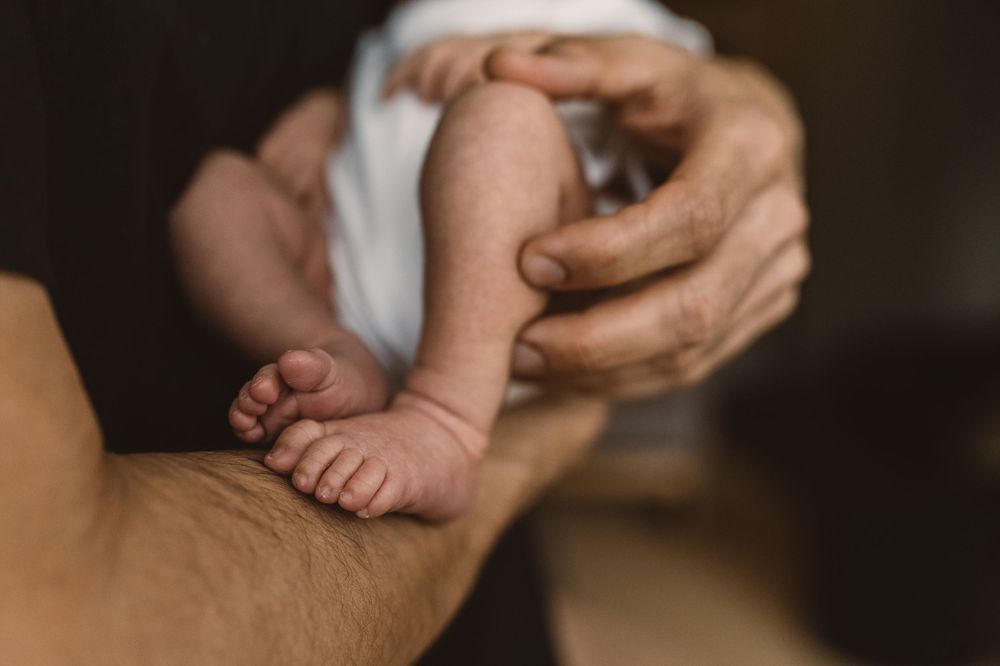 Close-up shot of hands gently holding and a tiny newborn baby's feet against a dark background.