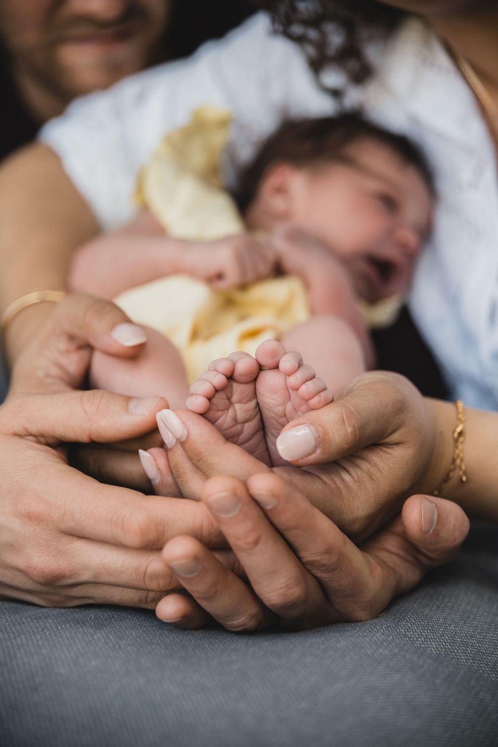 Gentle hands cradle tiny baby feet while newborn rests in soft yellow clothing.