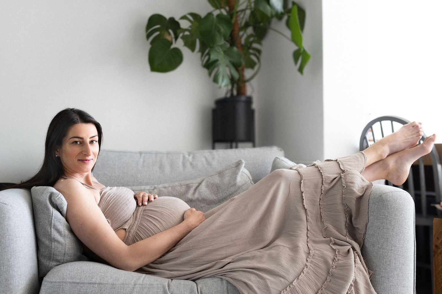 Person lying on gray couch with green plants in background showing signs of fatigue and exhaustion.