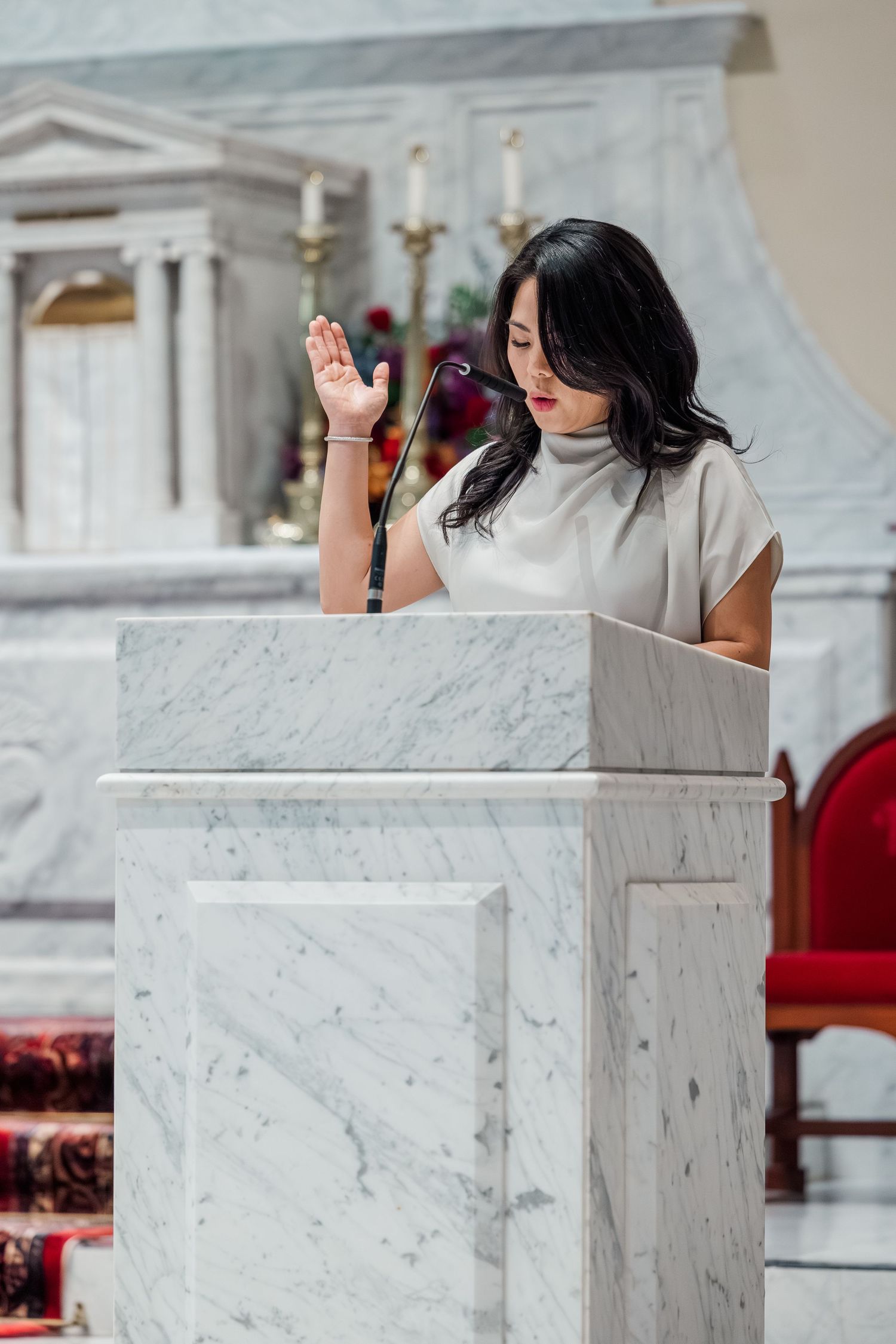 A speaker stands at a white marble podium during a presentation in an elegant interior space.