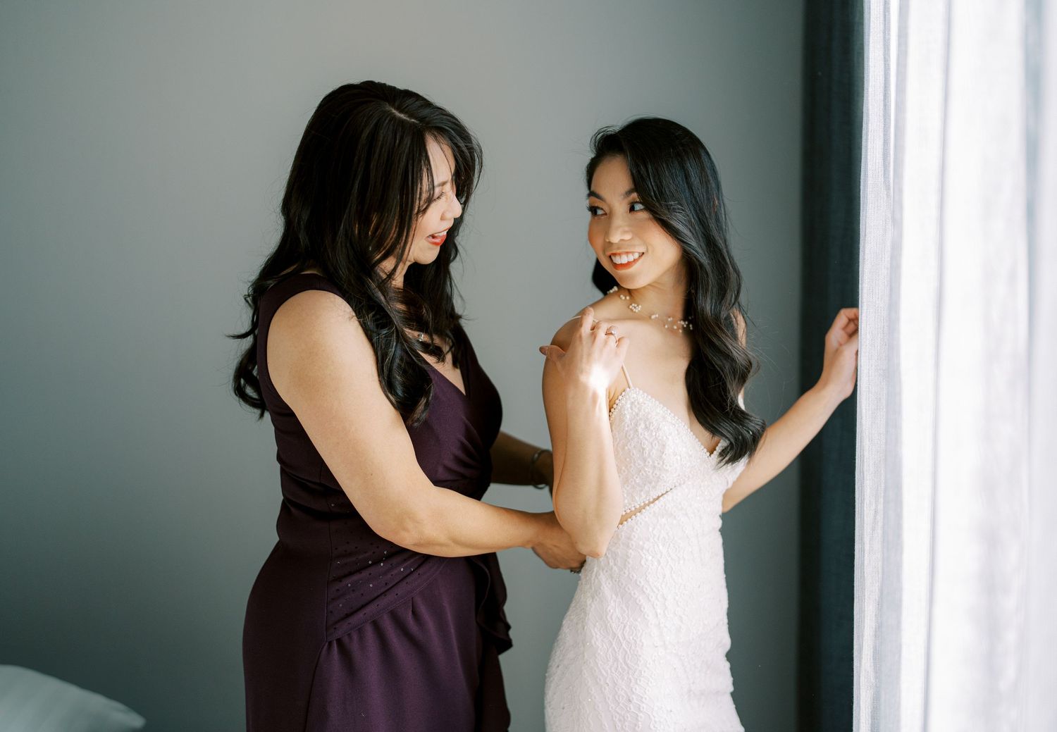 Two women in elegant dresses sharing an intimate moment near a window.
