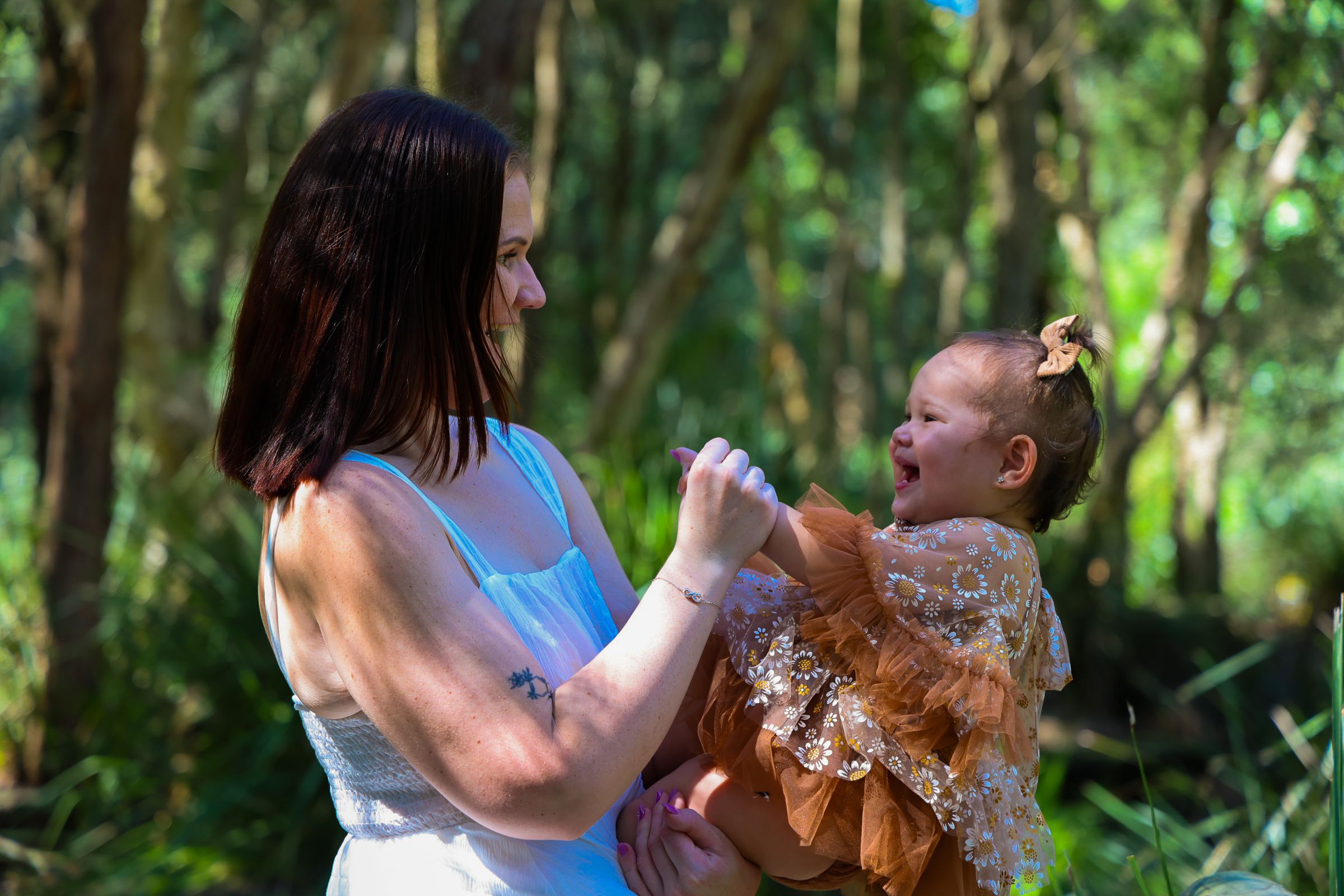Mum and daughter smiling at each other surrounded by bushland