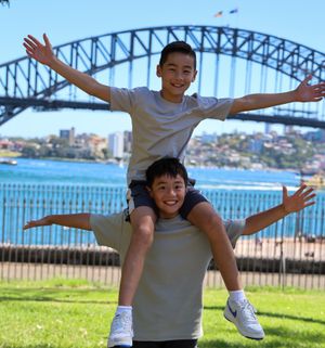 Two siblings, one balancing on another with the Sydney Harbour Bridge in the background